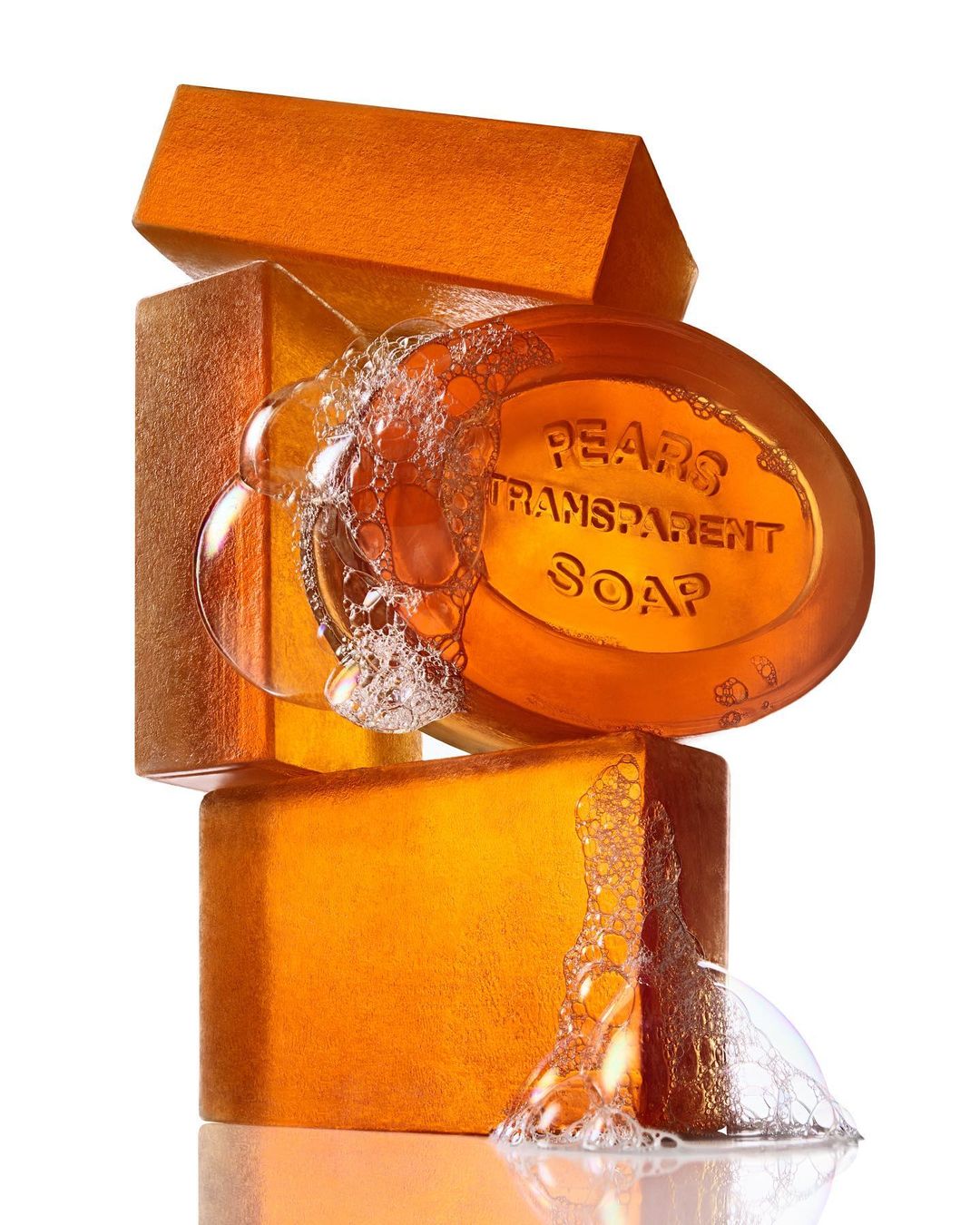 Close-up shot of a stack of translucent amber-colored Pears transparent soap bars with water bubbles, against a white background.