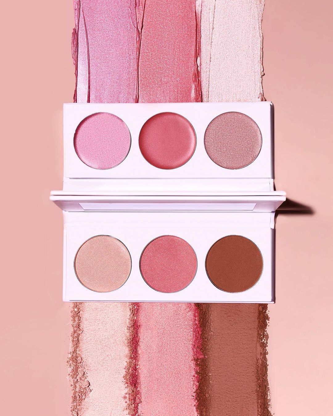 Two stacked makeup palettes featuring shades of pink and brown blush, presented on a matching pink surface with blush swatches.