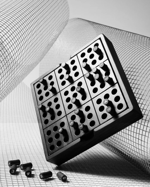 Black and white image of a wooden sudoku puzzle with cylindrical pieces, set against a mesh background, creating a graphic composition.
