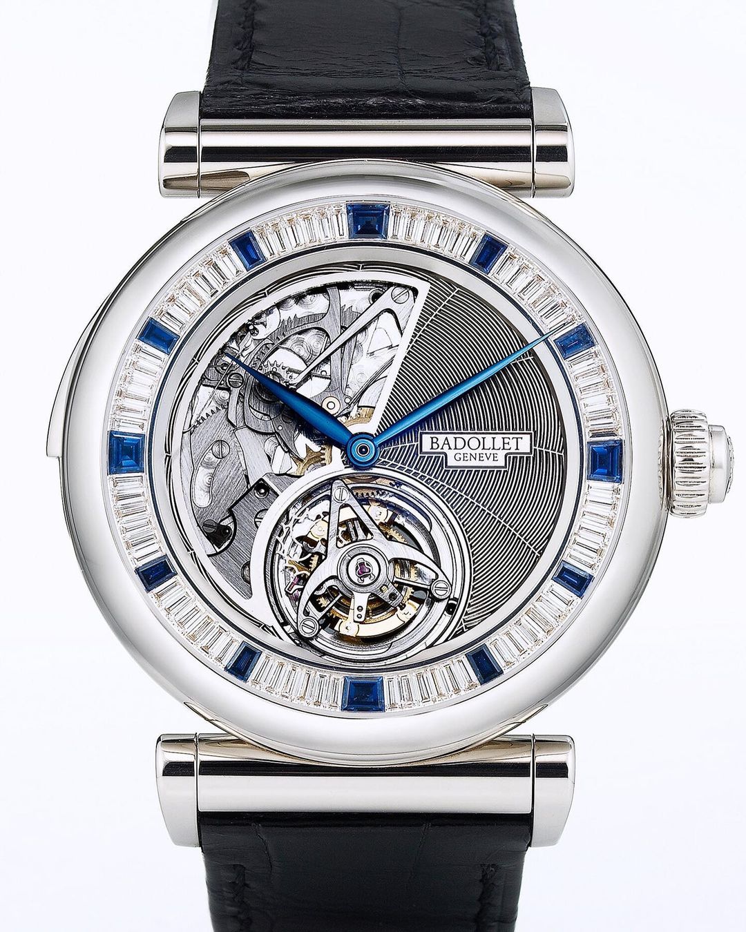 Silver Badollet Geneve wristwatch with a black leather strap features an open face and jewel accents, studio product shot.