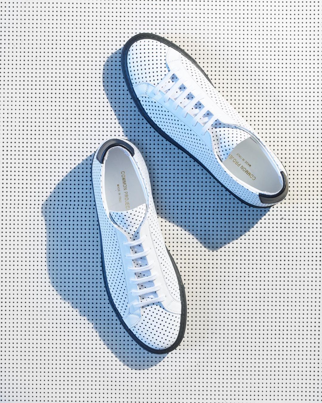 Overhead shot of two white leather Common Projects sneakers with black soles on a white background with black polka dots.