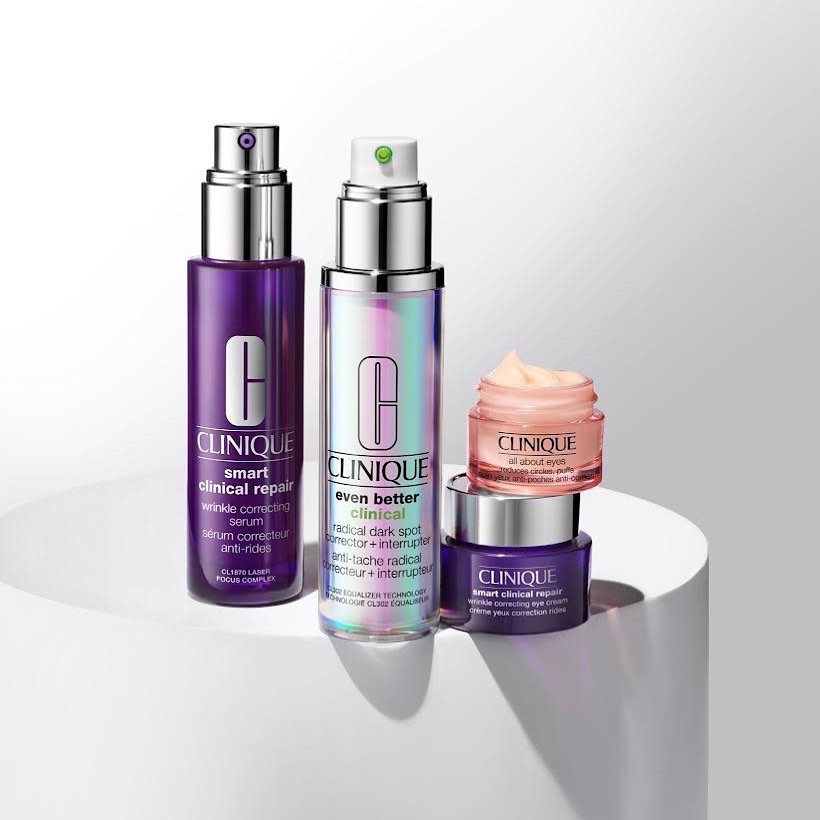 Clinique skincare product bottles and jars displayed on a white platform. Products include wrinkle correcting serum, dark spot corrector, eye cream.