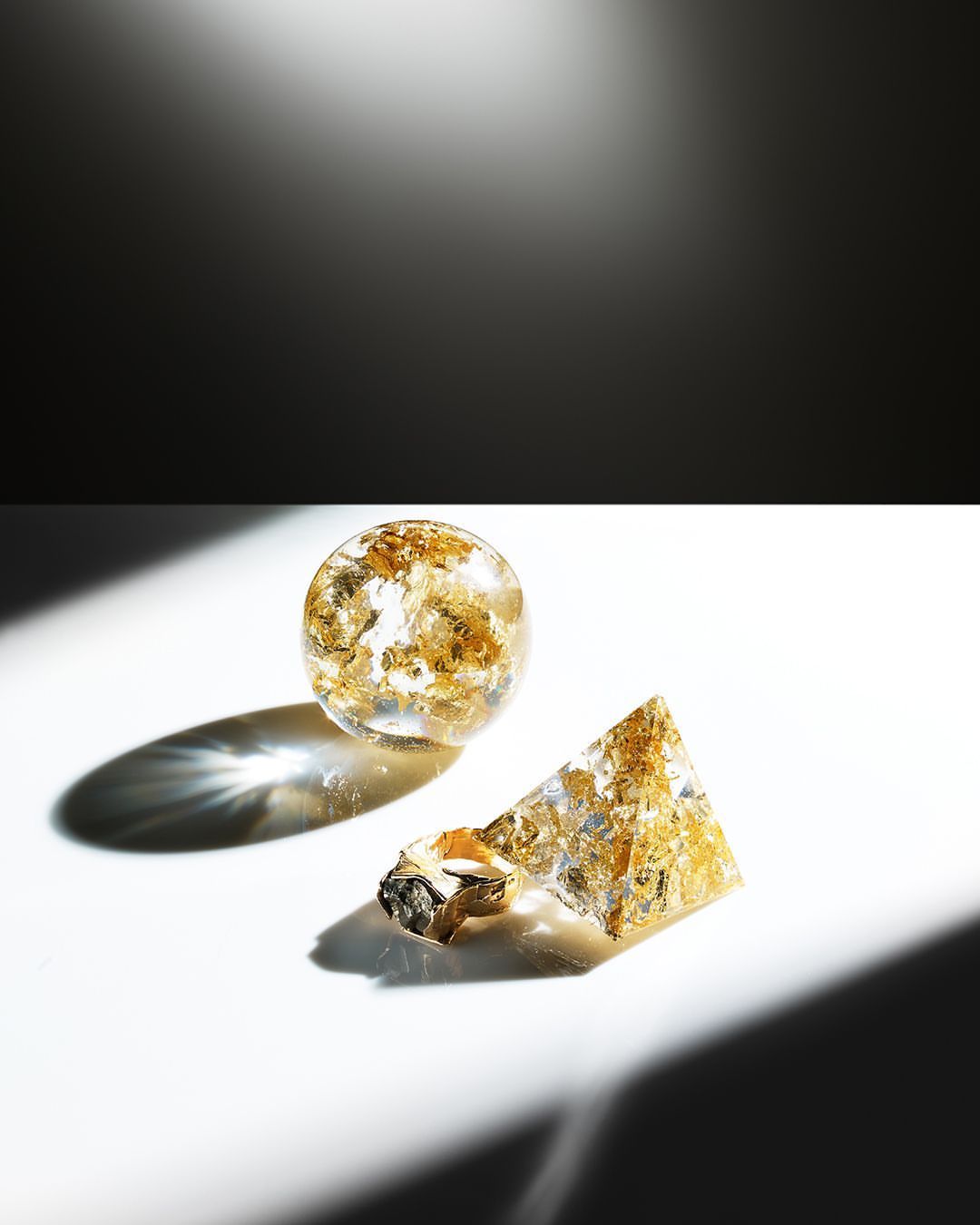 Resin art with golden foil flakes, featuring a round sphere and a triangular pyramid on a clean white surface, under studio lighting.