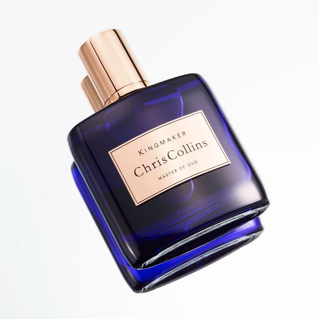 Close-up studio shot of a blue glass perfume bottle with a gold cap on a white background, showcasing its sleek design.