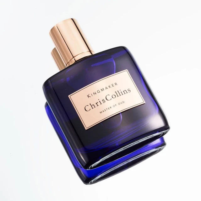 Close-up studio shot of a blue glass perfume bottle with a gold cap on a white background, showcasing its sleek design.