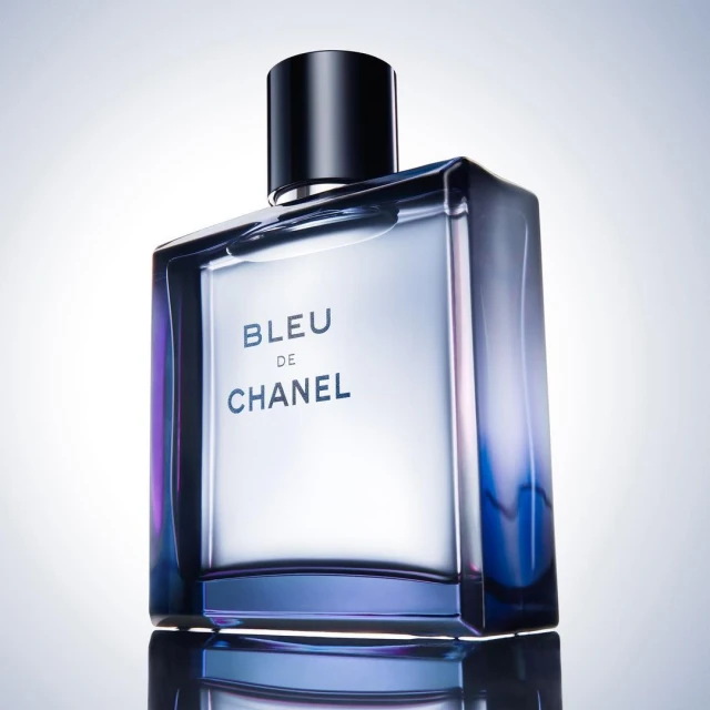 A sleek, reflective perfume bottle of Bleu de Chanel with a black cap, set against a bright gradient background, showcasing product design.