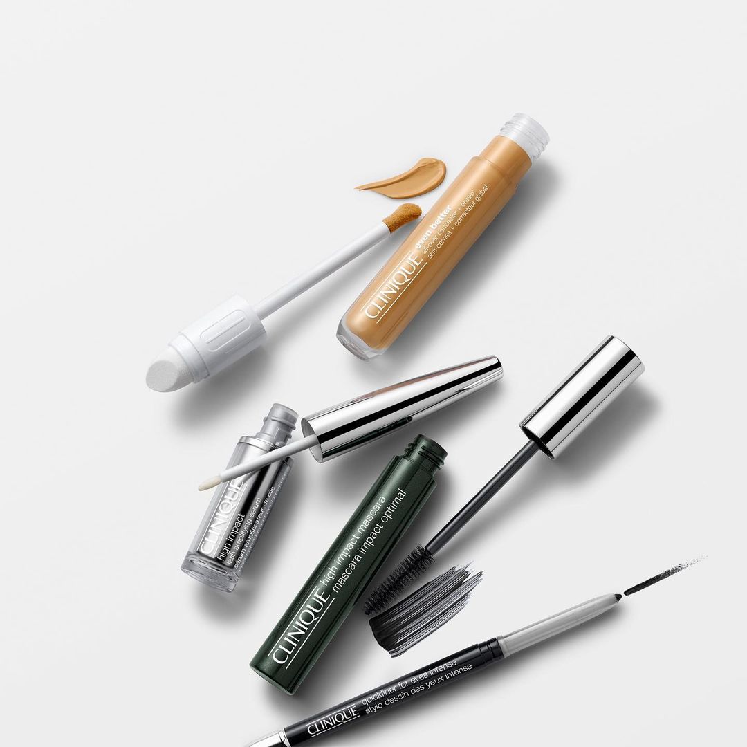 Still life of Clinique makeup products including concealer, mascara and eyeliner on a white background, shot in studio lighting.