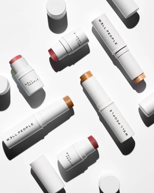 Close-up of several beauty stick applicators by W3ll People, displayed on a plain white background with soft shadows. Beauty product.
