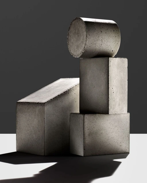 Abstract arrangement of geometric concrete shapes on a white surface against a dark gray background, creating a minimalist studio composition.