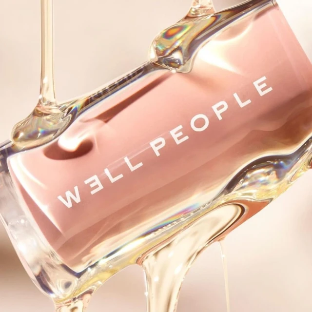 Product shot of a pink Well People product with honey or syrup pouring over it in a studio setting with a neutral background.