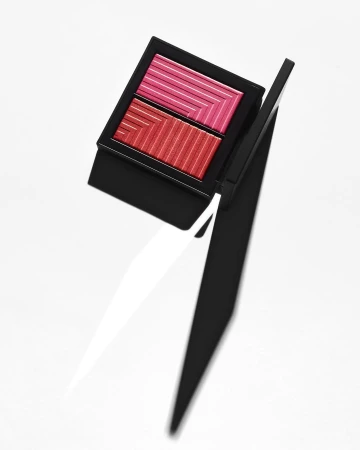 An open compact case with dual pink and red ribbed powder blush compartments against a plain white background.