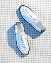 Overhead product photograph of two perforated white low-top sneakers resting on a textured grey perforated metal background with sharp shadows.