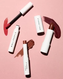 Flat lay of cosmetic products including lipsticks and liquid gloss tubes with matching makeup swatches on a pink textured background.