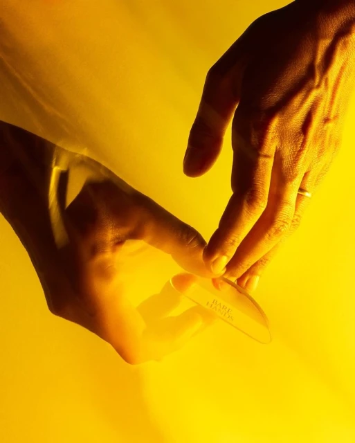 Close-up of two hands holding a clear skincare tool against a vibrant yellow backdrop, highlighting skin tones and product details.