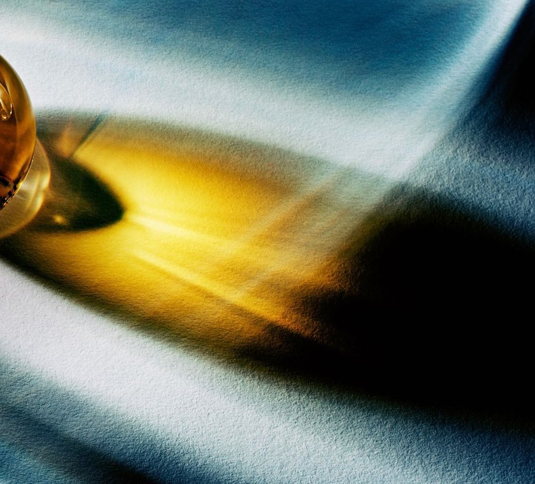 Amber liquid in a glass creates an abstract shadow on a textured surface, casting a warm, golden glow against the cool backdrop.