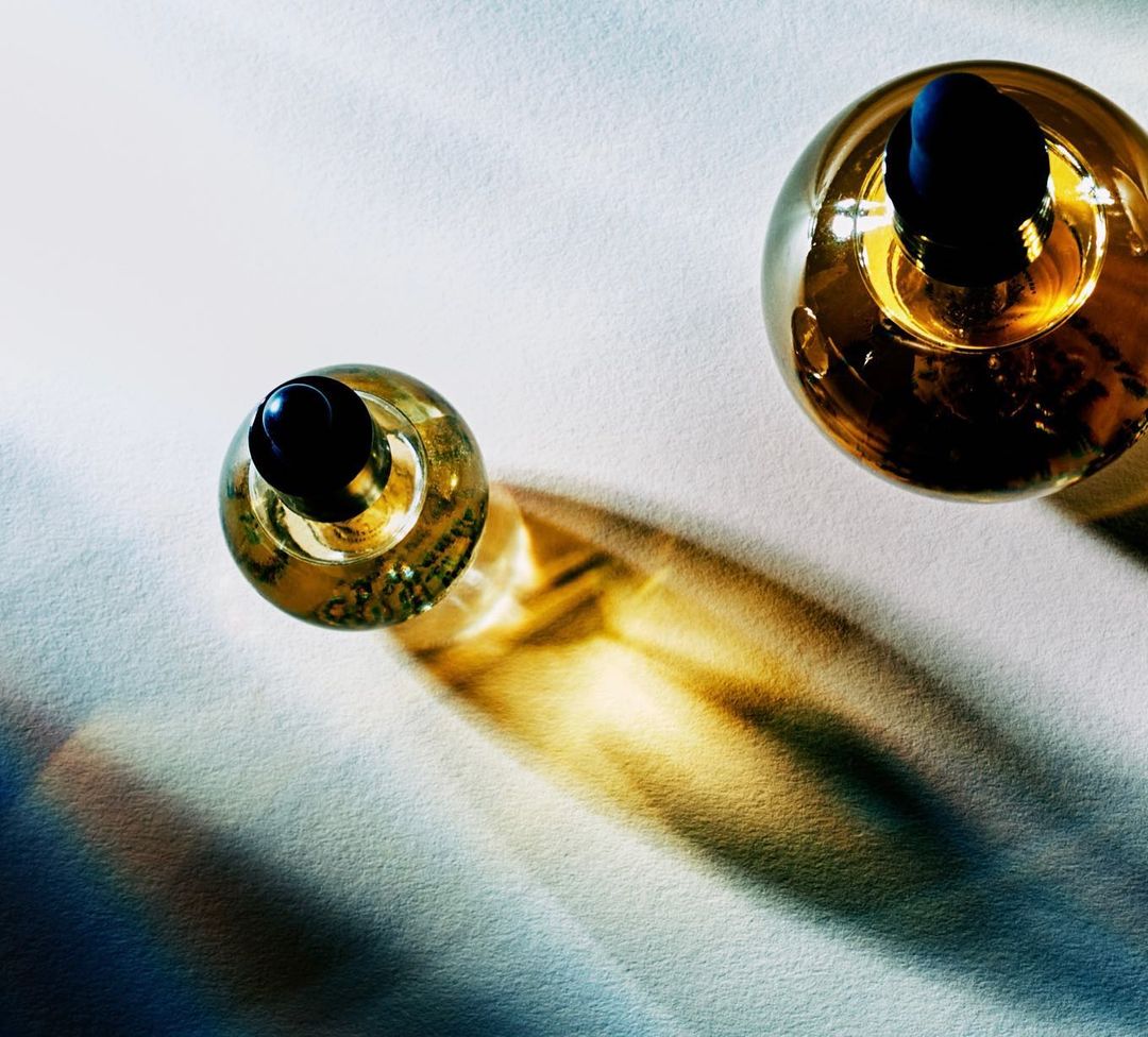 Overhead shot of two glass bottles filled with amber liquid and black caps on a white surface with dramatic lighting creating golden shadows.