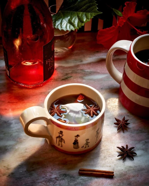 Close-up of a ceramic mug filled with dark liquid and star anise, sitting on a marble surface, with a wine bottle in the background.