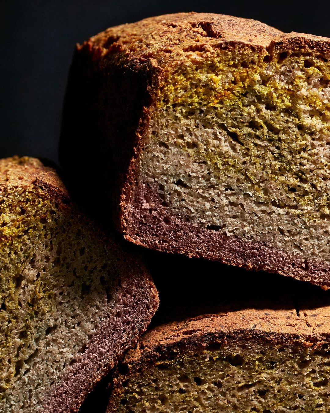 Close-up of sliced sourdough bread with a dark crust and colorful interior layers, against a dark background with shadow and texture.
