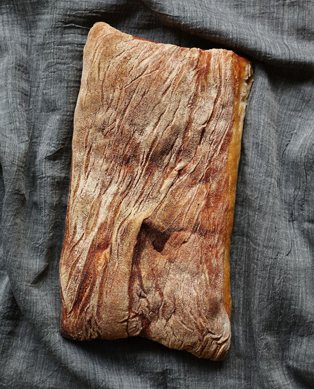 Close-up of rectangular sourdough bread loaf on a gray linen surface with visible crust texture and golden-brown color.