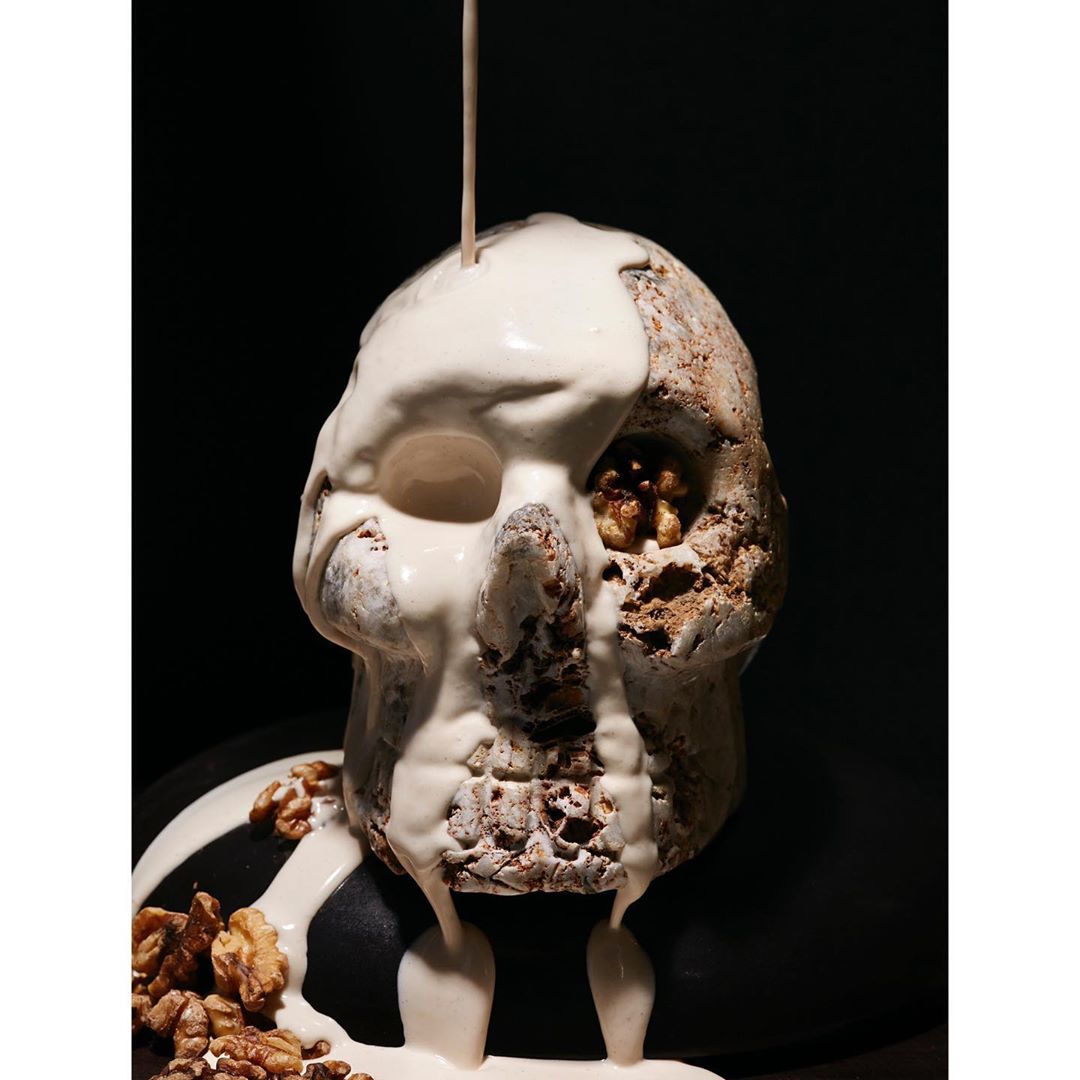 A skull with dripping white substance and walnuts sits against a black backdrop, offering a stark contrast and intriguing texture.