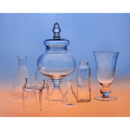 Collection of clear glass vessels and a miniature acrylic chair arranged on a surface against a blue and orange gradient background.