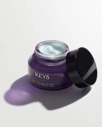 Purple cosmetic jar with a black lid resting beside it on a white surface, revealing pale cream inside