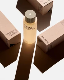Cylindrical body wash bottle standing upright surrounded by three matching product boxes casting long sharp shadows on white background.
