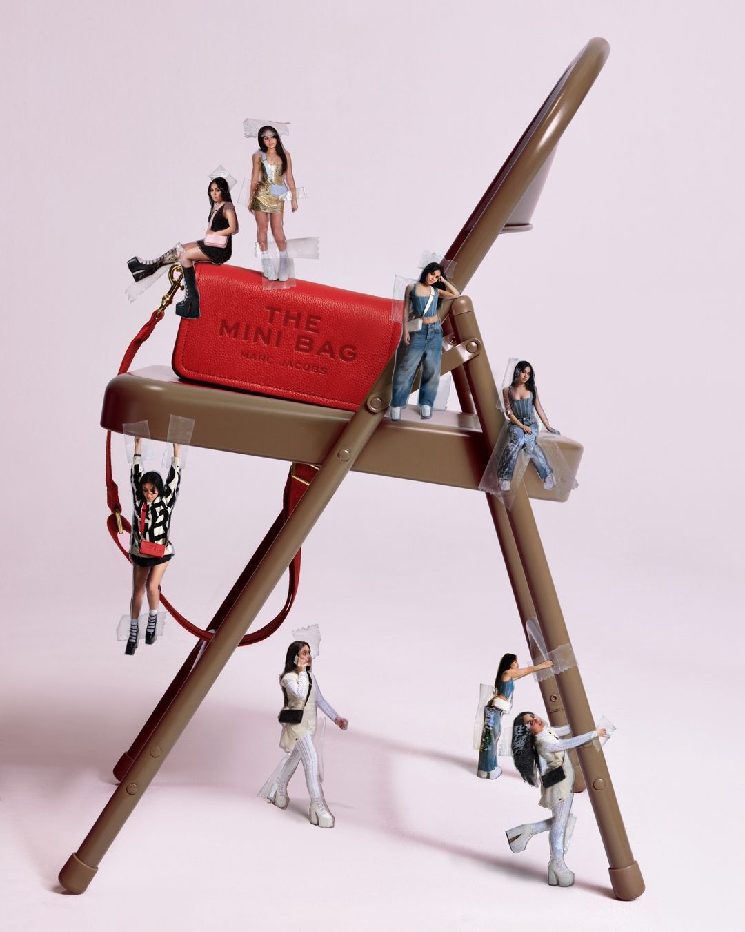 Red Marc Jacobs Mini Bag on a brown folding chair with miniature paper figures taped to it in a studio setting. 