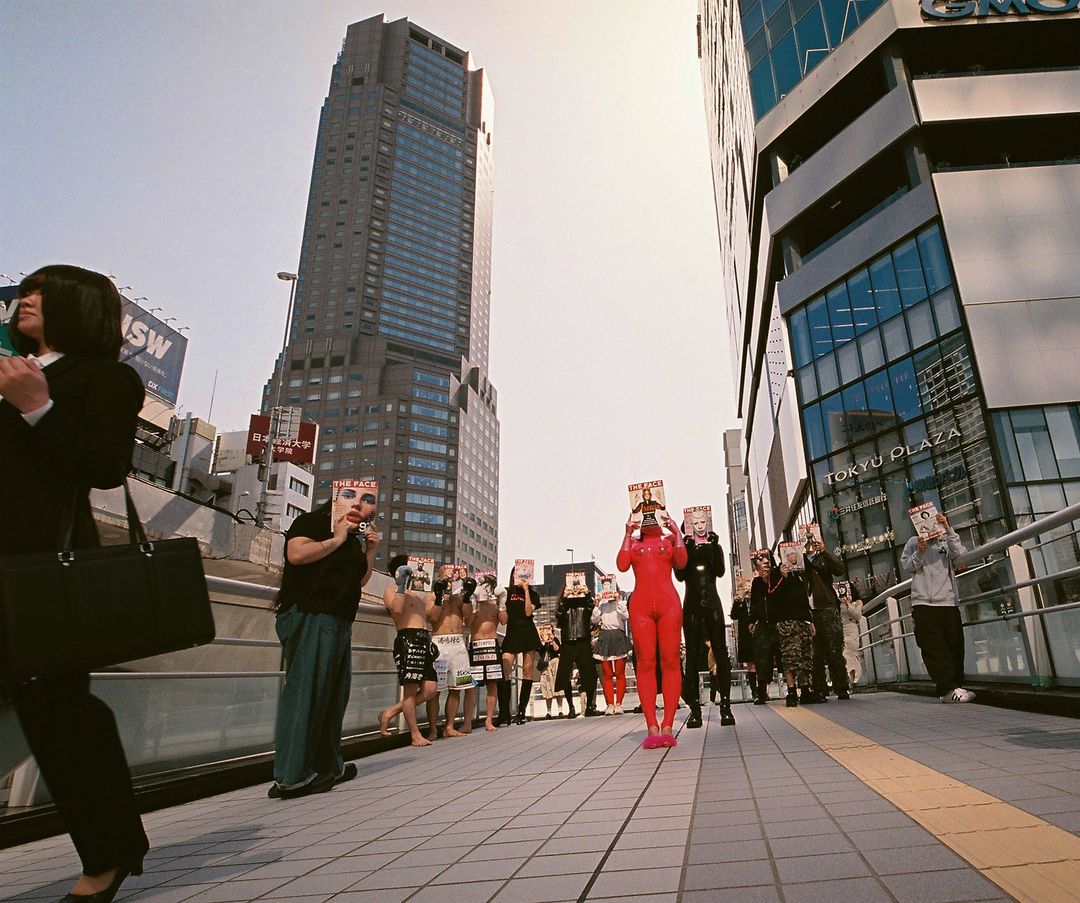 A group of people holding face masks in an urban setting, with modern buildings in the background, creating a staged scene.