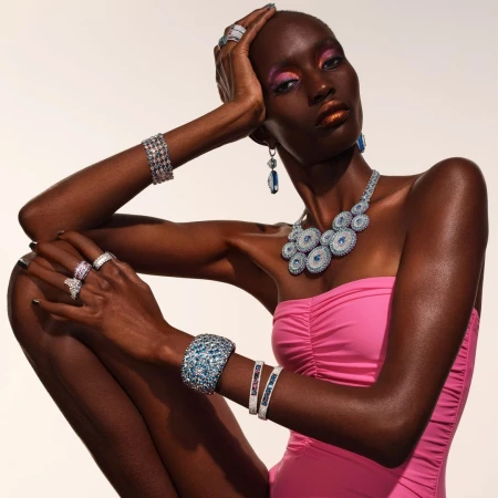 Black woman wearing pink top adorned with crystal necklaces, bracelets, and rings, captured in a portrait by John-Paul Pietrus