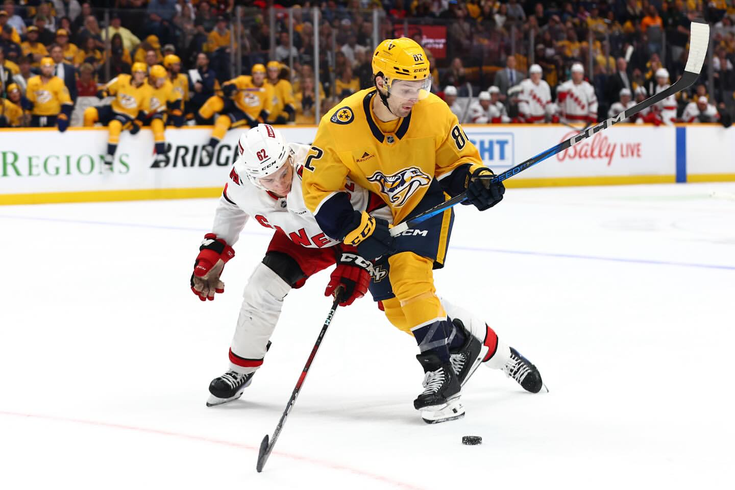 Intense ice hockey game action shot featuring two male players in team jerseys, helmets, and protective gear battling for puck possession.
