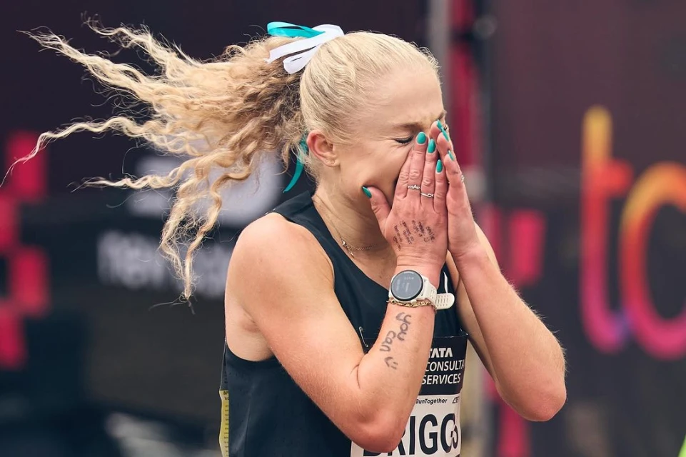 Emotional female marathon runner covering face in tears, wearing athletic wear and a watch, with curly blonde hair in a ponytail.