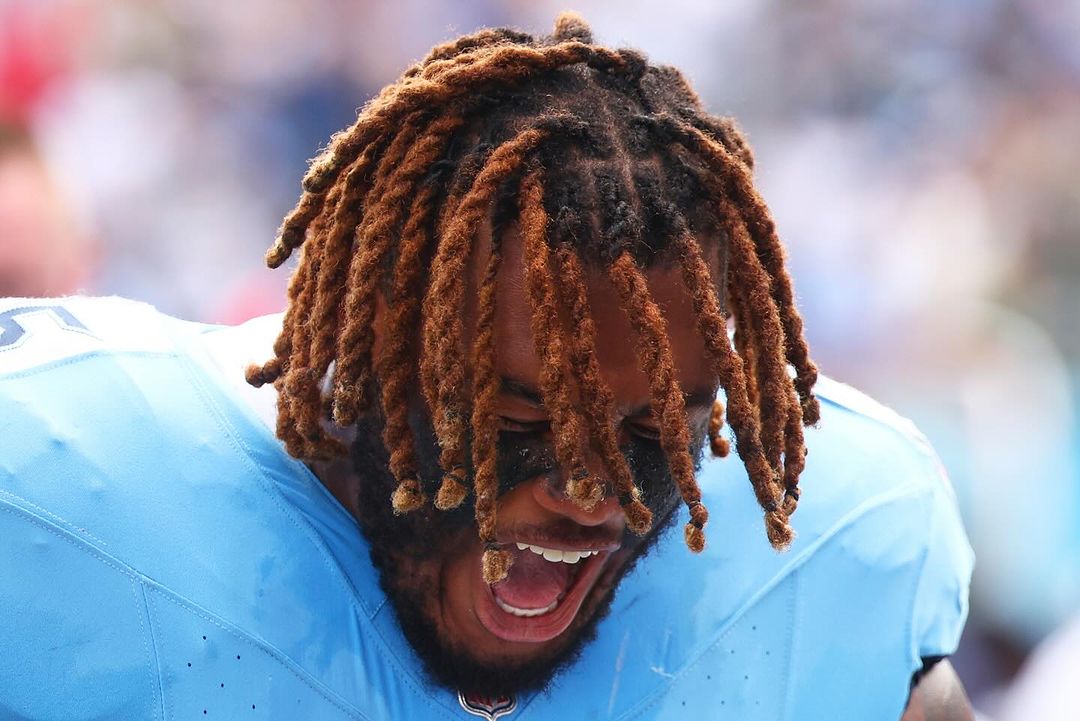 Close-up of an adult male athlete with dreadlocks and black eye paint, wearing a blue sports jersey with an open mouth.