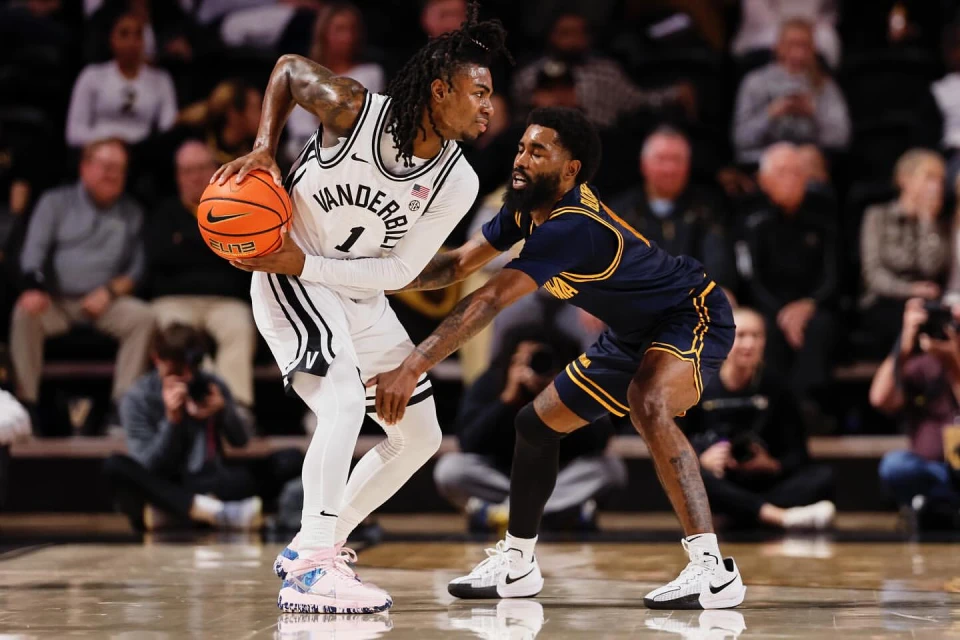 Two basketball players face off on an indoor court; one dribbles the ball while the other defends in this action-packed sports scene.