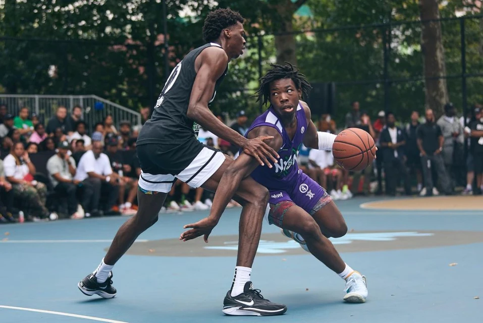 Two young men face off in an intense basketball game on an outdoor court surrounded by spectators, showcasing athletic prowess and competitive spirit.