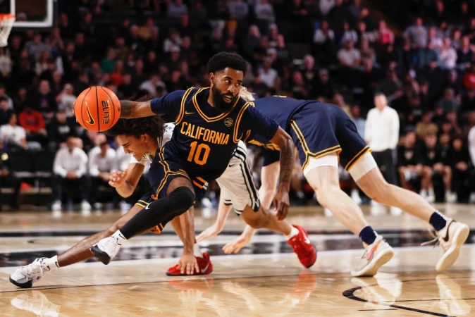 Basketball player with the ball dribbling on the basketball court in a navy and gold uniform; a crowd watches in the background.