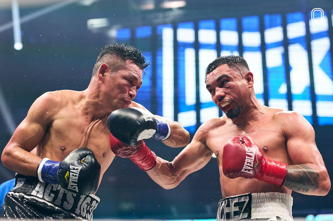 Two male boxers in the ring, exchanging punches during a match. The fighters are wearing boxing gloves and shorts, with an intense expression.