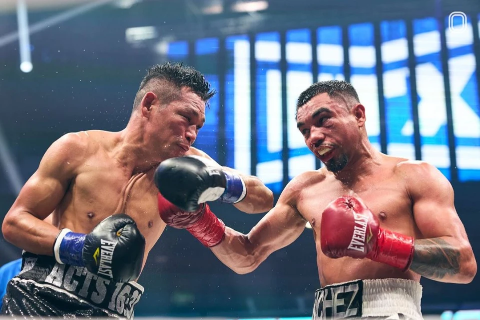 Two male boxers in the ring, exchanging punches during a match. The fighters are wearing boxing gloves and shorts, with an intense expression.