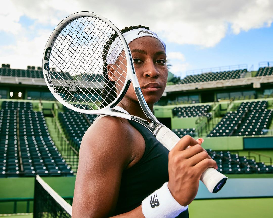 Portrait of a female tennis player in sportswear with a tennis racket over her shoulder, set on the tennis court bleachers.