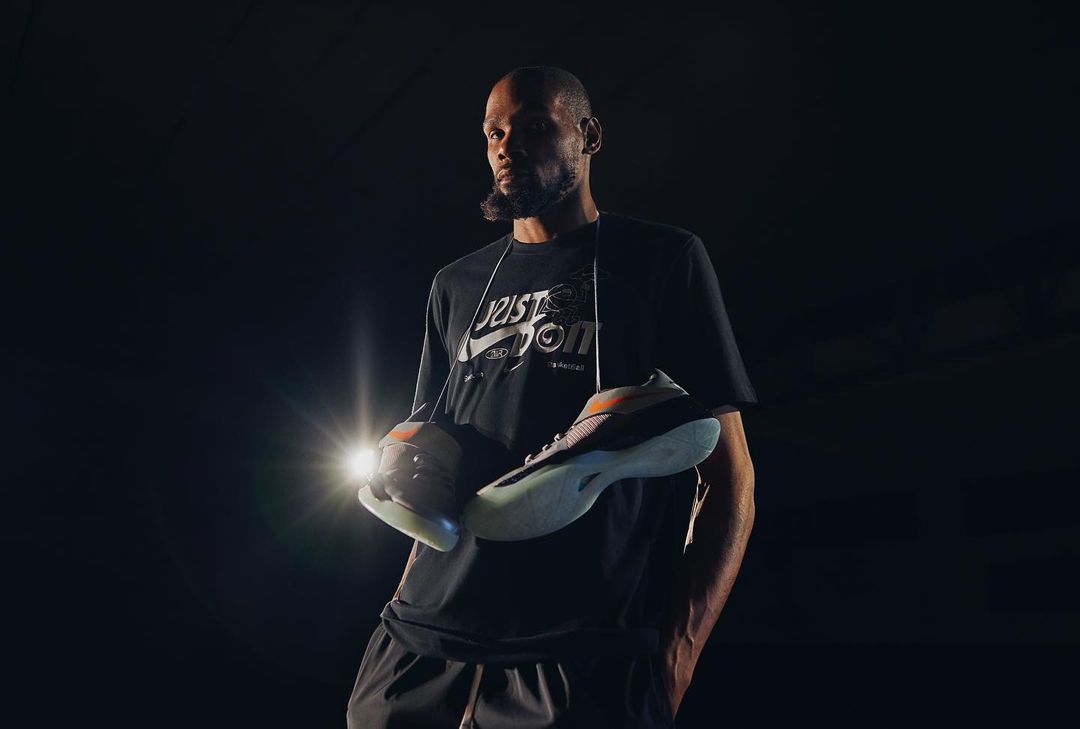 Athletic man holds Puma RS-Metric sneakers in photo studio spotlight. Black tee and shorts. Dark backdrop. Sport, fashion concept.