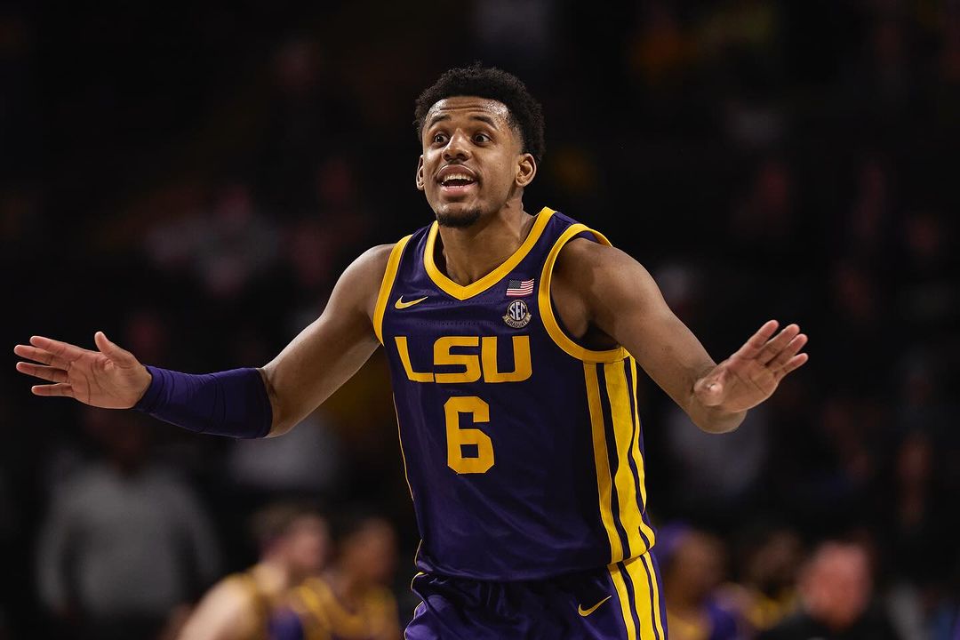 A basketball player in a purple and yellow LSU jersey stands with arms outstretched, looking up during a basketball game.