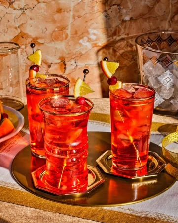 Three red cocktails with orange slices and cranberries on golden coasters on a tray by Johnny Autry