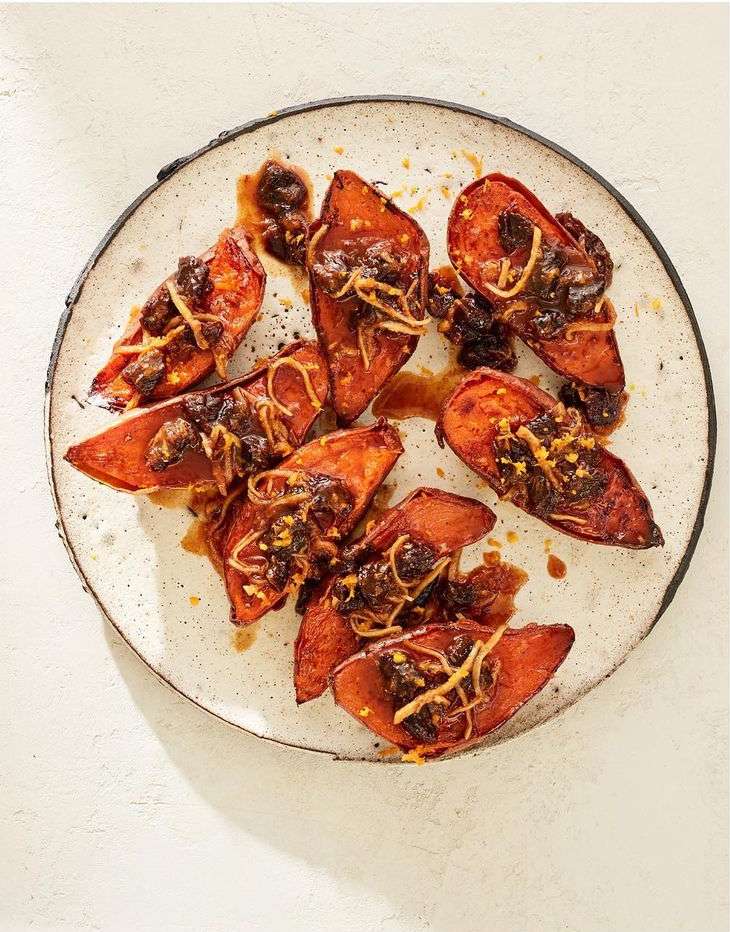 Overhead shot of glazed sweet potato wedges topped with onions on a speckled ceramic plate, against a white background.
