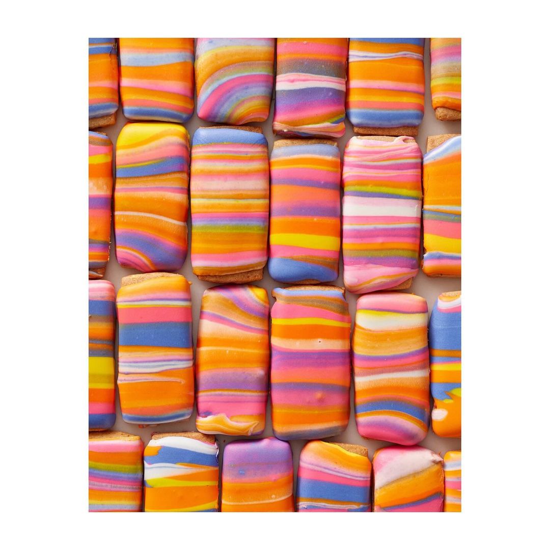 Close-up of colorful, striped sugar cookies with orange, pink, purple, and blue frosting in a flat lay, food photography style.