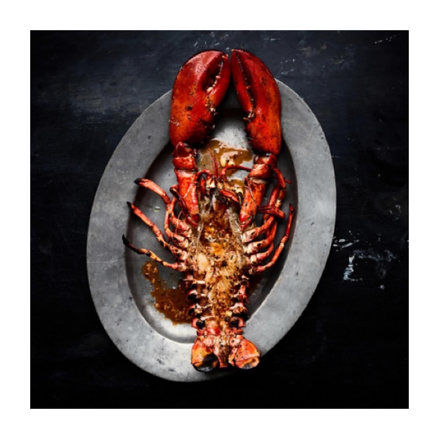 Overhead shot of a cooked lobster on a silver platter against a dark background, showcasing its vibrant red color and textured shell.