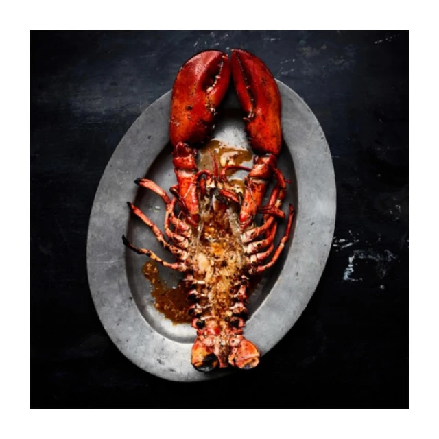 Overhead shot of a cooked lobster on a silver platter against a dark background, showcasing its vibrant red color and textured shell.