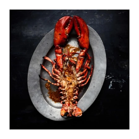 Overhead shot of a cooked lobster on a silver platter against a dark background, showcasing its vibrant red color and textured shell.