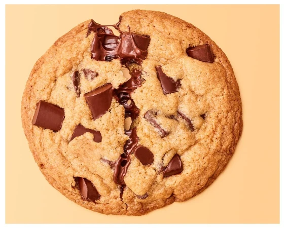 Top-down shot of a chocolate chip cookie with melted chocolate chunks on a light orange background, perfect for food and dessert-themed projects.