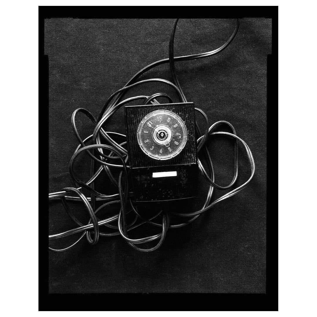Monochrome photograph showcasing a vintage rotary telephone, complete with its cord, set against a textured, dark backdrop.