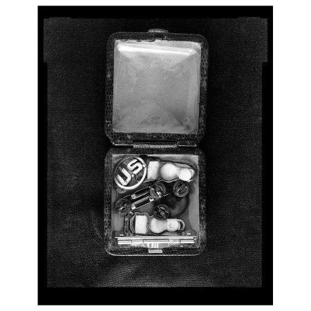 Black and white studio shot of an opened box containing U.S. military insignia, badges, and pins against a dark fabric backdrop.